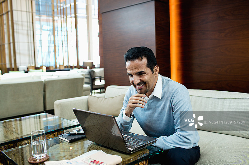 一个微笑着在酒店用笔记本电脑的男人。图片素材