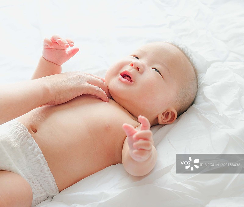 一个刚出生的亚洲婴儿在床上喝着奶瓶里的牛奶，可爱的黑眼睛婴儿躺在床上，一个孩子躺在床上休息图片素材