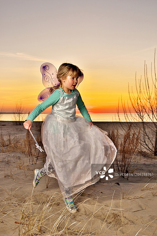 年轻的女孩打扮成一个仙女在日落海滩试图飞翔图片素材
