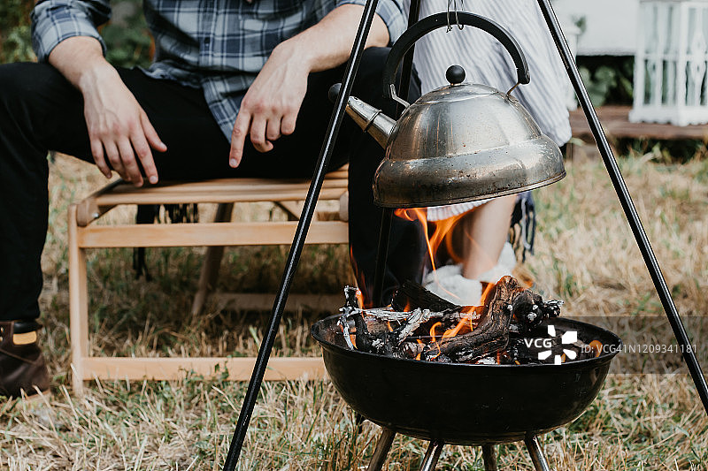 一个男人和一个女人在露营时，正在看篝火上烧开的水壶。图片素材
