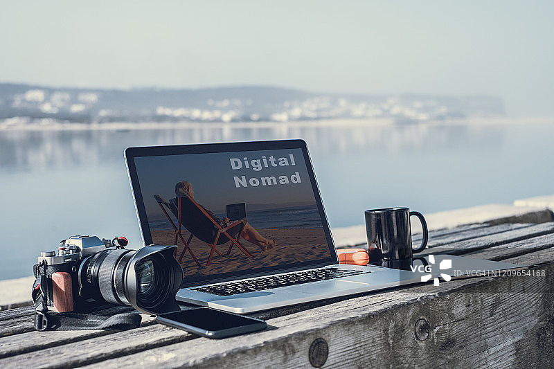 数字游牧民-长椅上放着笔记本电脑和相机，背景是大海图片素材