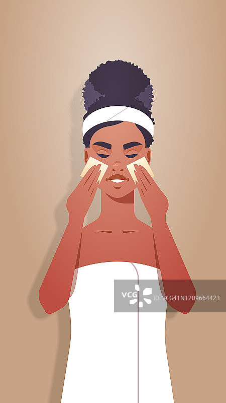 年轻女子用海绵涂抹粉底霜，穿着毛巾非洲裔美国女孩清洁和护理她的脸护肤spa放松面部护理概念肖像垂直图片素材
