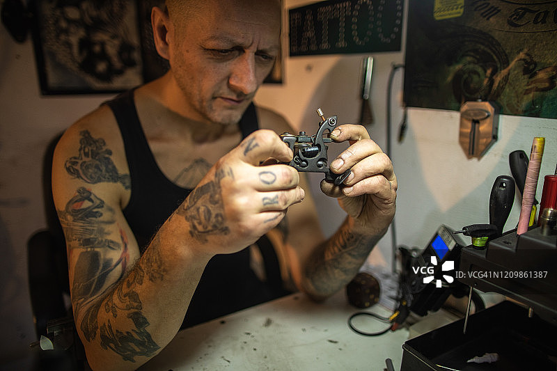 纹身艺术家坐在他的工作台上，看着他的纹身机图片素材