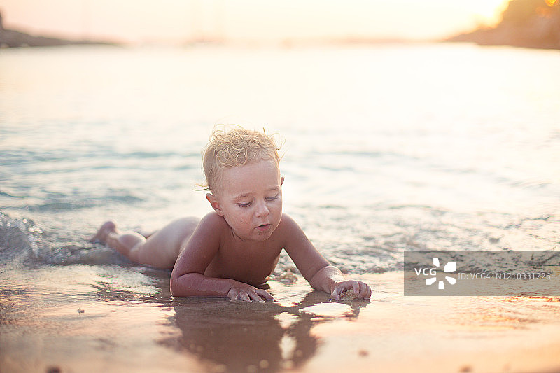 蹒跚学步的孩子在日落时躺在海里玩沙子图片素材