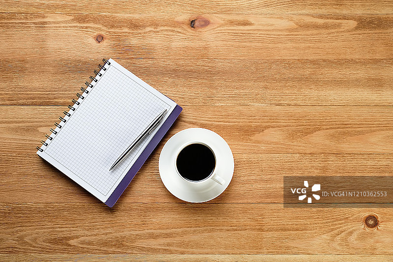 一支笔在一张空白的记事本上，一杯黑咖啡在一张木桌上。商人或经理在工作场所的物品。图片素材