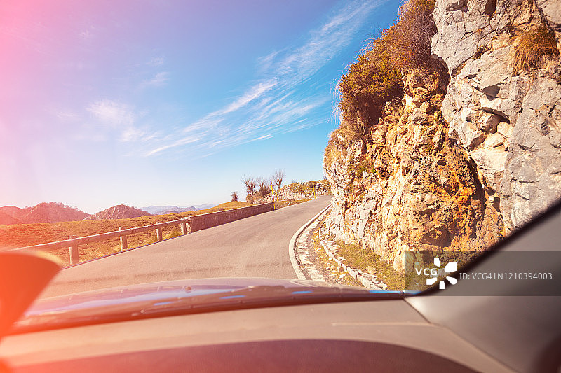 在一个阳光明媚的日子里，透过挡风玻璃可以看到美丽的山景。在欧罗巴国家公园蜿蜒的山路上开车。坎塔布里亚、西班牙、欧洲图片素材