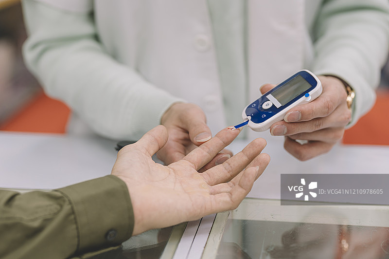 一名亚洲华人药剂师正在一名男性病人的手指上做糖尿病测试图片素材