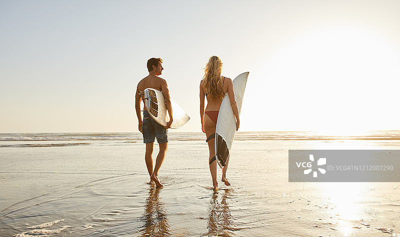 年轻夫妇穿着泳衣，带着冲浪板去海边图片素材