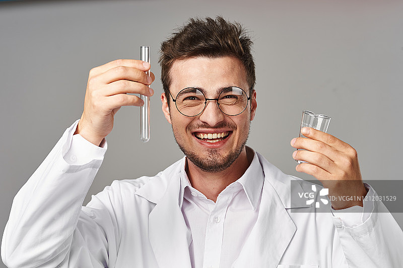 一幅巨大的肖像，一个实验室助理穿着白大褂，戴着圆眼镜，手里拿着一个试管和一杯试剂图片素材