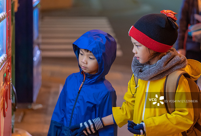 两个孩子晚上在仙台车站附近的日本自动售货机选购饮料。图片素材