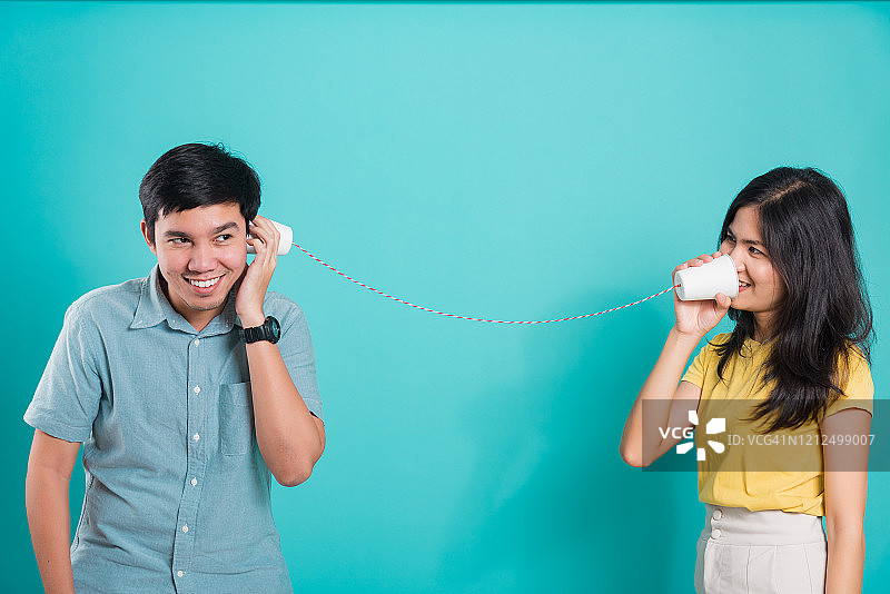 幸福的亚洲年轻夫妇美丽英俊的微笑和聊天一起纸可以电话在一个工作室拍摄在蓝色的背景图片素材
