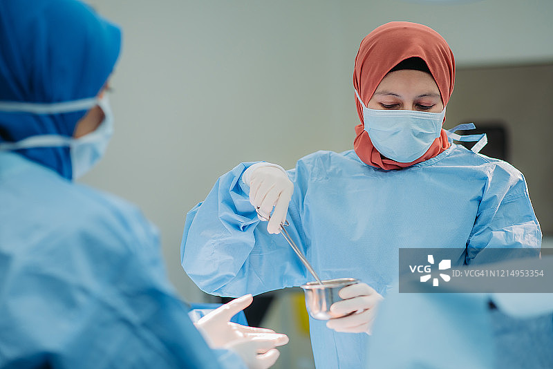 亚洲马来族女外科医生和护士在医院的手术室用钳子准备消毒水图片素材