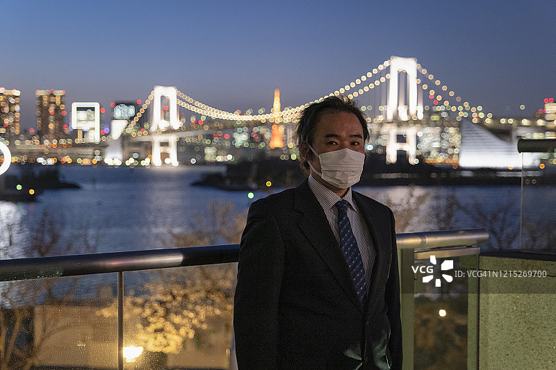 中年日本商人戴着面具看着相机与东京天际线在背景图片素材