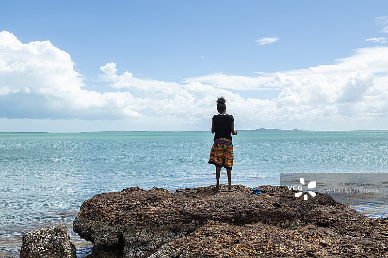 年轻的土著妇女站在岩石上在浩瀚的海洋中捕鱼图片素材