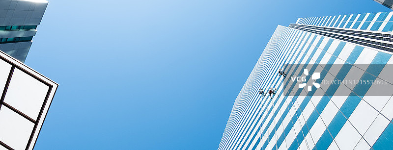 一组工人清洁高层建筑摩天大楼的窗户在蓝色的天空图片素材