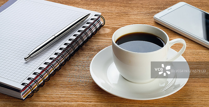 采购产品手机，笔和记事本的笔记，咖啡杯，在一个木头桌子上。一个商人或经理在工作场所的工作主题。图片素材
