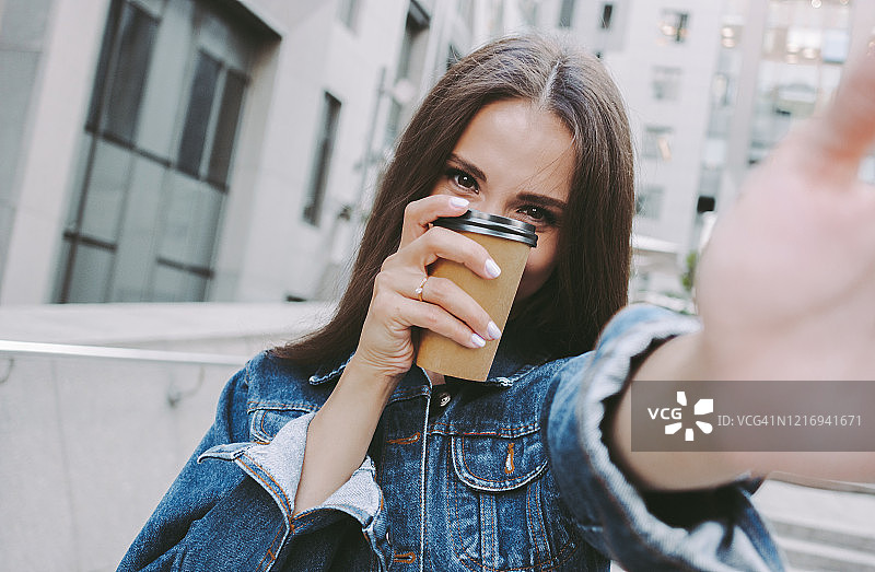 可爱的女孩在相机上自拍，手里拿着咖啡图片素材