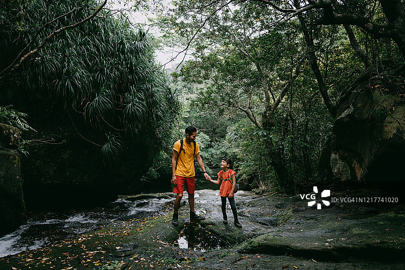 父亲和女儿徒步通过河流的丛林，冲绳，日本图片素材