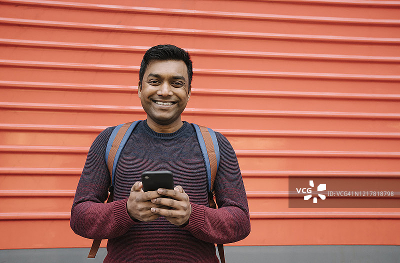 一名微笑的男子手持红色背景的智能手机图片素材