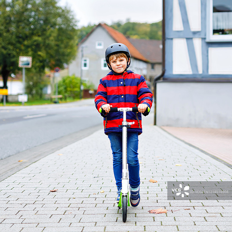 可爱的小男孩戴着头盔骑着滑板车在公园里。儿童在冬天、春天或秋天进行户外活动。滑稽快乐的孩子穿着五颜六色的时装。图片素材