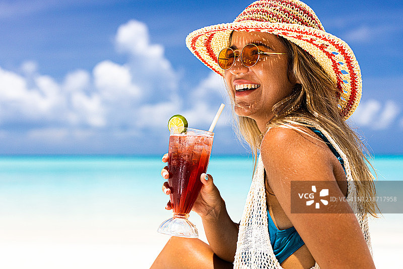 年轻快乐的女人在夏日的海滩上喝着鸡尾酒。图片素材