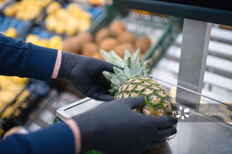 男子的手在保护手套把菠萝在一个杂货店的重量图片素材