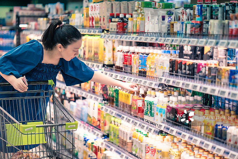 亚洲孕妇在超市购物，选择酱在瓶子图片素材