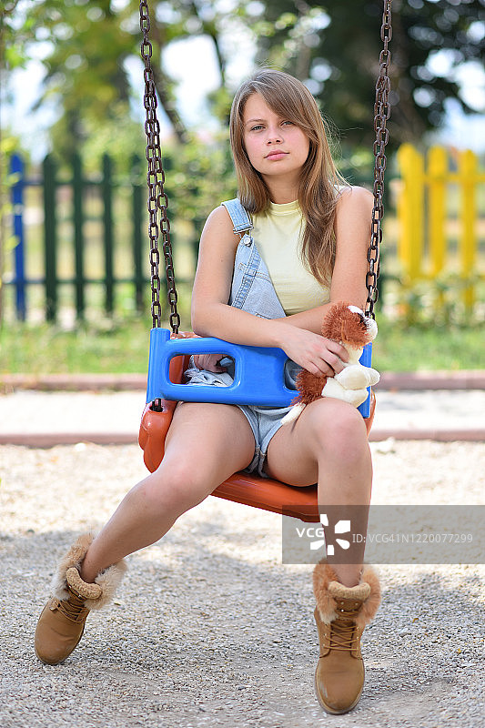 悲伤和单身年轻美丽的女人爱上小狗娃娃在公园的秋千图片素材