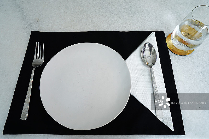 近桌布置白瓷陶瓷板，不锈钢餐具和一杯泉水图片素材