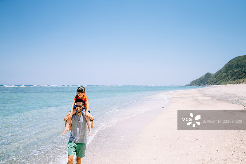 父亲背着孩子在热带海滩上跑步图片素材