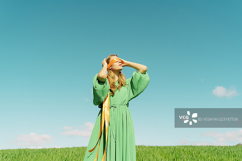 蒙住眼睛，穿着绿色连衣裙的年轻女子站在田野里图片素材