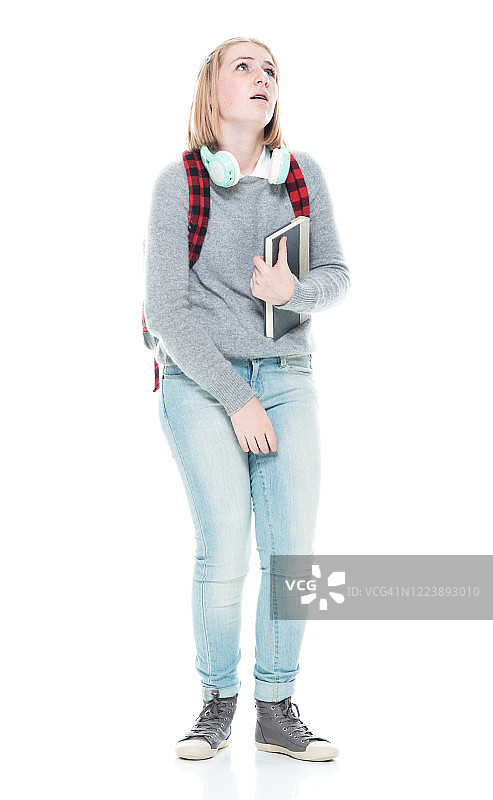 白色背景前的年轻女学生穿着马球衫，拿着书，戴着耳机图片素材