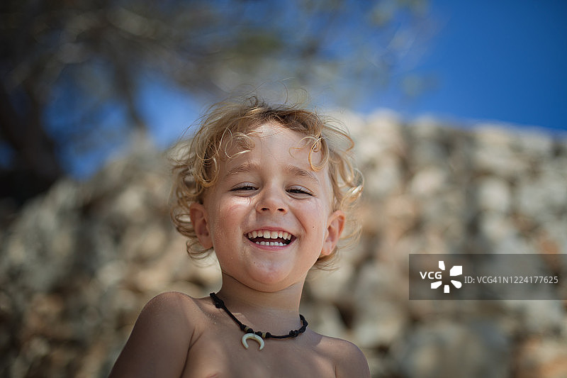 男孩在海滩的一堵石墙前露出露出牙齿的微笑图片素材