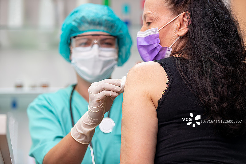 女医生穿着防护工作服清洗年长妇女接种疫苗后的手臂图片素材
