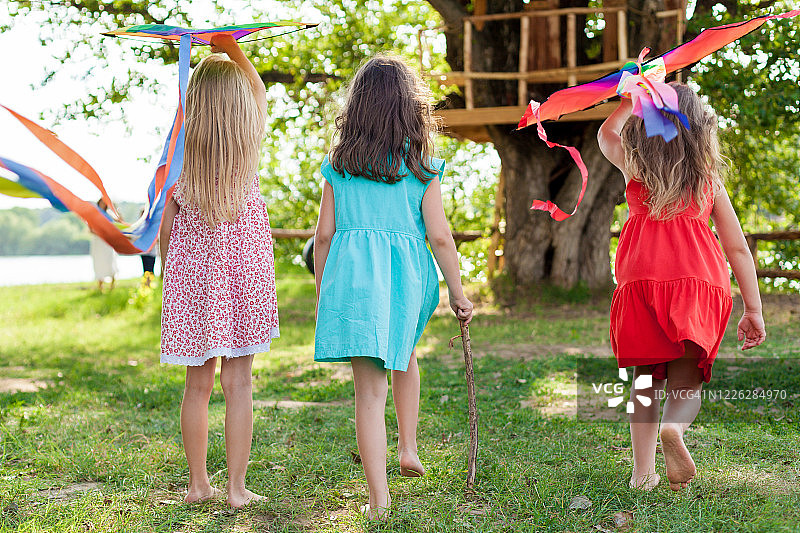 孩子们在户外玩风筝，日落，在夏天的一天。和朋友一起度过有趣的时光。快乐的小女孩们放风筝。孩子们有趣的夏季游戏图片素材