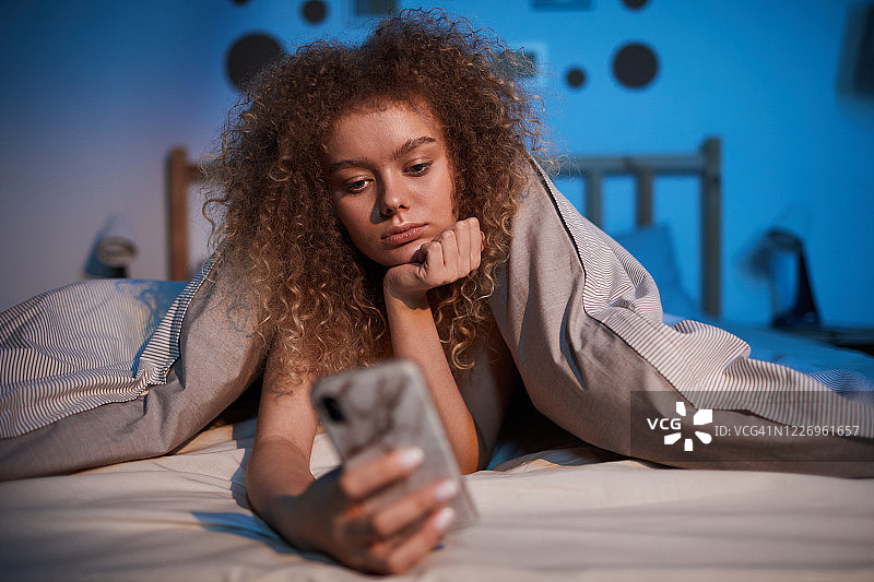 无聊的年轻女人在床上使用智能手机图片素材