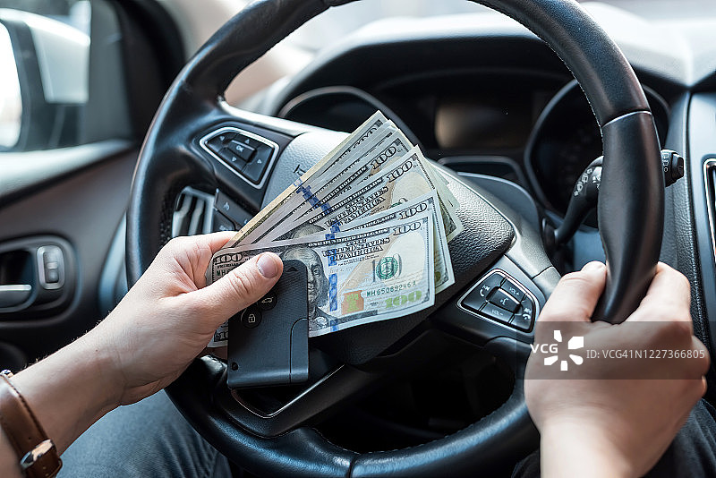 男人为旅行租了一辆车，手里拿着美元和自动钥匙图片素材