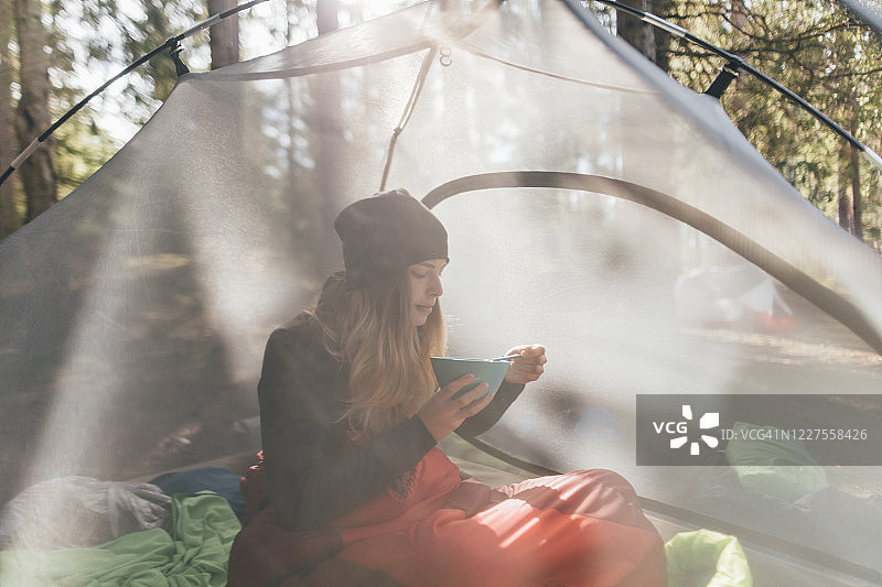 年轻女子坐在帐篷里，在森林里吃早餐图片素材