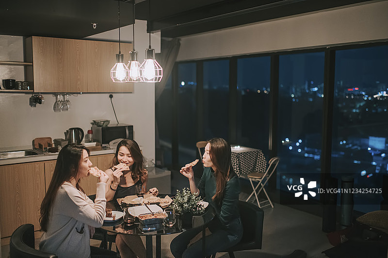 一群亚裔中国女性朋友在公寓里社交聚会，晚上在餐厅吃披萨图片素材
