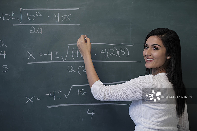 年轻女子微笑着在黑板上写数学方程图片素材