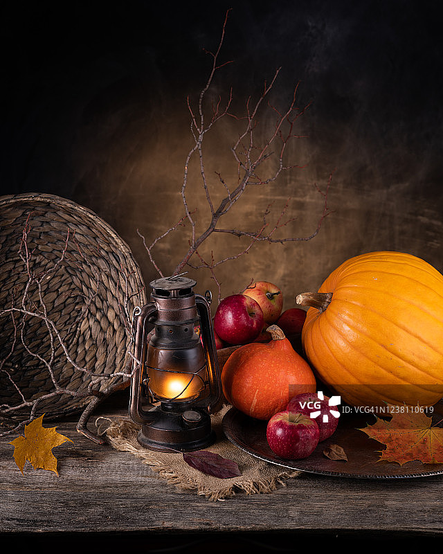 秋天情绪的概念。收获静物南瓜、苹果、煤气灯、黄色枫叶。旧的木桌上。图片素材