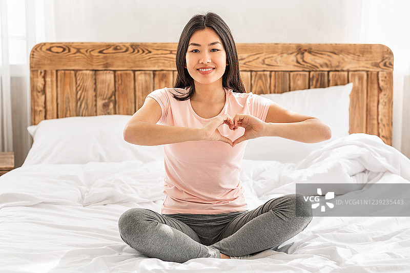 亚洲女人在家里的床上做心形手势图片素材