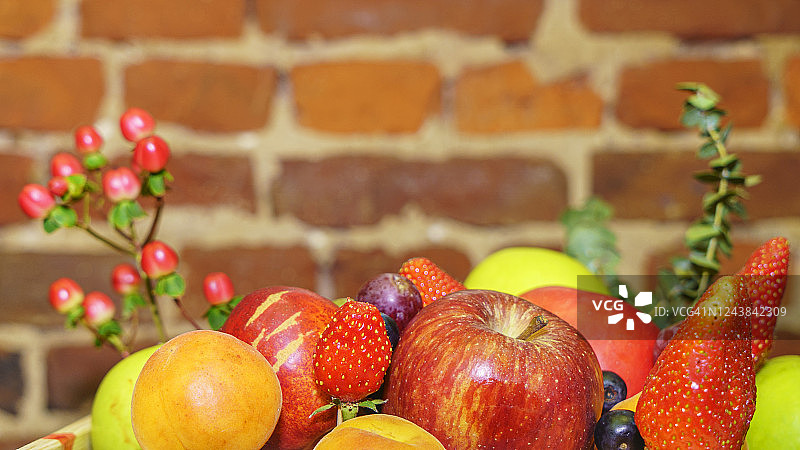 木盒里的一套浆果和水果。苹果，草莓，葡萄，浆果和桃子在散焦的红砖背景。图片素材