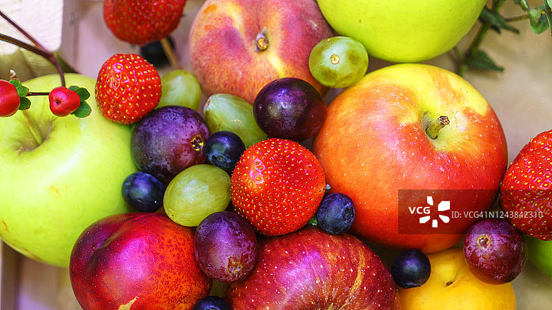 木盒里的一套浆果和水果。红砖背景上点缀着苹果、草莓、葡萄、浆果和桃子。图片素材