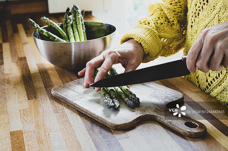 一个妇女用菜刀在木砧板上切芦笋图片素材