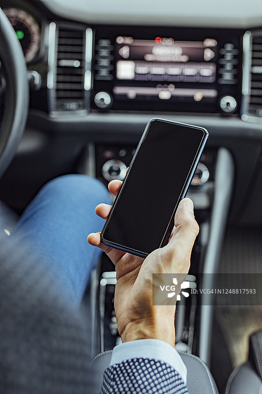 汽车里的科技:一个商人坐在驾驶座上发短信(空白屏幕，拷贝空间)图片素材