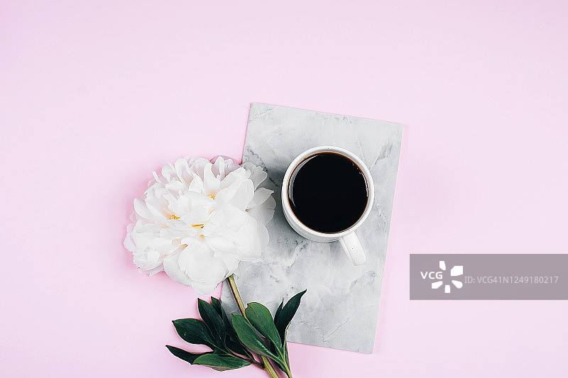 咖啡杯，笔记本和白色牡丹花在粉红色的桌子背景。舒适，静物，简约的概念。俯视图，平放，复制空间图片素材