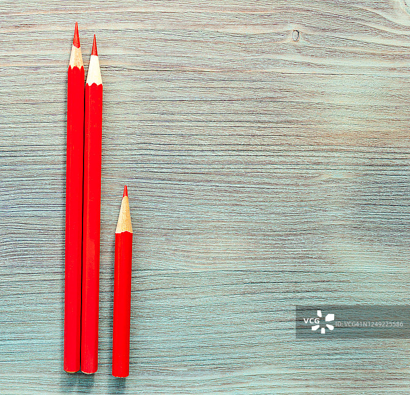 两根长红铅笔，一根短在绿松石蓝色天然木桌的背景上拉近。俯视图图片素材