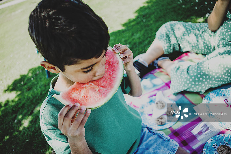 男孩(7)在下午和家人野餐时吃西瓜片图片素材