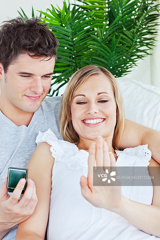 高兴的女人看着她的戒指躺在她的男友在客厅图片素材